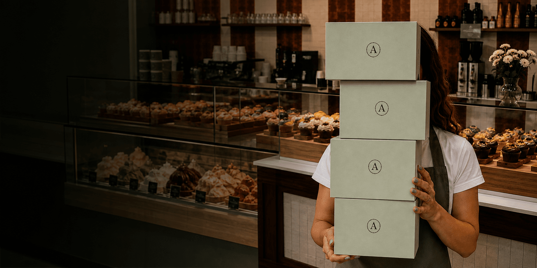 Artisan staff member holding sage pastry boxes at the café counter